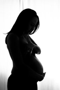 Gegenlicht-Silhouette einer schwangeren Frau mit einem Fenster, das sanftes Licht spendet.