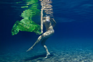Eine Frau in einem Bikini tanzt im Wasser mit einem grünen Tuch, festgehalten mit einem Unterwasserfoto.