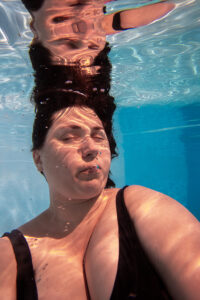 Portrait einer Frau mit geschlossenen Augen, befindet sich unter Wasser in einem Pool und lässt sich von der Schwerelosigkeit treiben.