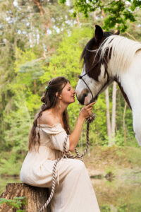 Eine Frau in einem weißen Kleid küsst sanft ein Pferd auf die Nüstern.
